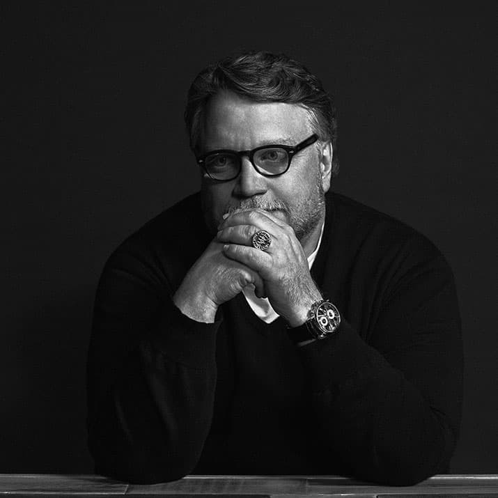 Guillermo del Toro director de cine in a black-and-white portrait, seated with hands clasped and thoughtful expression.